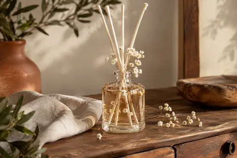 Diffuseur à bâtonnets en flacon de verre, accompagné de fleurs de gypsophile conservées sur un meuble en bois