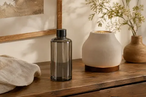 Flacon gris de recharge Jasmin Précieux posé sur une console en bois près d’une lampe catalytique