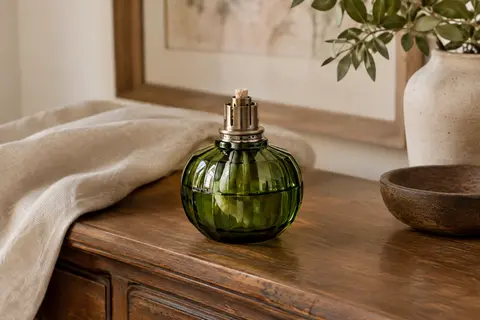 Lampe catalytique en verre vert avec brûleur métallique posée sur une console en bois patiné.